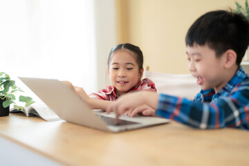 Cute girl and boy sitting in the classroom and doing homework together. Girl looking at laptop and smile play game with her friend. Learning, education and kindergarten concept. Back to school