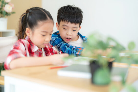 Cute girl and boy sitting in the classroom and doing homework together. Boy looking at friend on her drawing. Portrait of school kid. Learning, education and kindergarten concept. Back to school