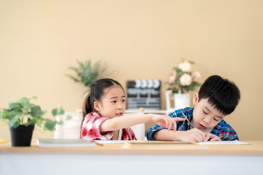 Cute girl and boy sitting in the classroom and doing homework together. Girl ask her friend pick up color pencil. Portrait of school kid. Learning, education and kindergarten concept. Back to school.