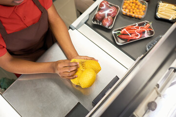Above angle of young African American saleswoman holding packed fresh lemons over counter while weighing them and scanning