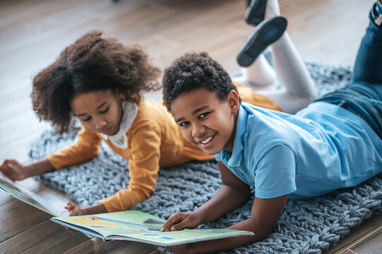 Two kids lying on the floor and reading a book