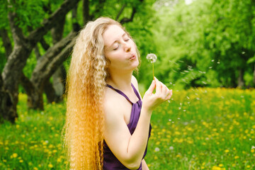 Obraz premium red-haired woman with a dandelion in her hands in an apple orchard among flowering dandelions