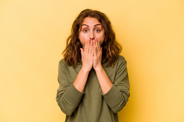 Young caucasian woman isolated on yellow background shocked, covering mouth with hands, anxious to discover something new.