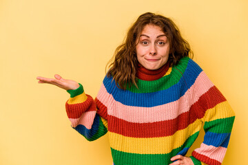 Young caucasian woman isolated on yellow background showing a copy space on a palm and holding...