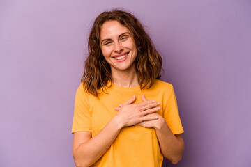 Young caucasian woman isolated on purple background has friendly expression, pressing palm to...