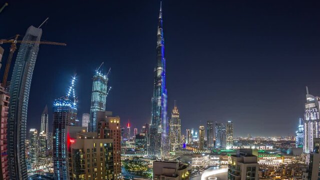 Panorama of Dubai Downtown cityscape with tallest skyscrapers around aerial night timelapse. Construction site of new towers and busy roads with traffic from above