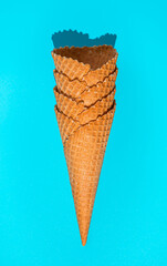 A stack of waffle ice cream cones on a blue background in hard light. Top view, vertical.