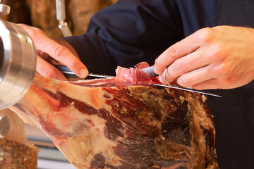 Butcher cuts shavings of Spanish serrano ham in the foreground