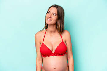 Young caucasian pregnant woman wearing bikini isolated on blue background dreaming of achieving goals and purposes
