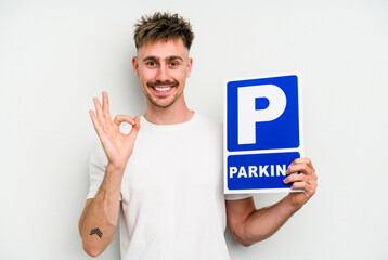 Young caucasian man holding parking placard isolated on white background cheerful and confident showing ok gesture.