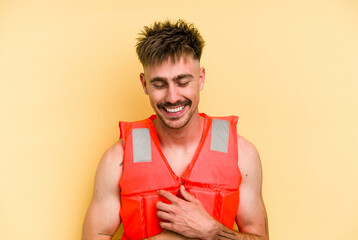 Young caucasian man wearing a life jacket isolated on yellow background laughing and having fun.