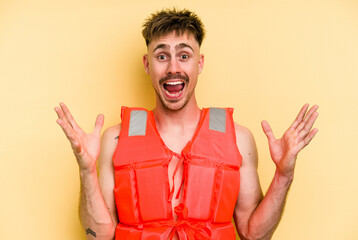 Young caucasian man wearing a life jacket isolated on yellow background receiving a pleasant...