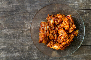 Fried chicken in sauce in a glass plate on a dark wooden table.