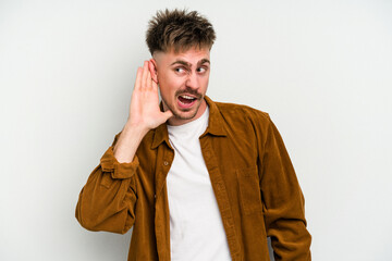 Young caucasian man isolated on white background trying to listening a gossip.