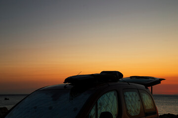 Surfboard attached to the top of a car at sunrise.