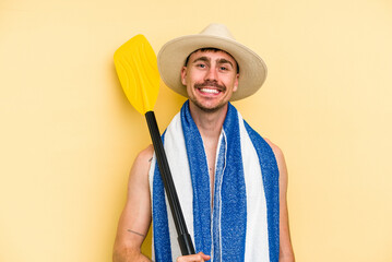 Young caucasian man holding rowing stick isolated on yellow background