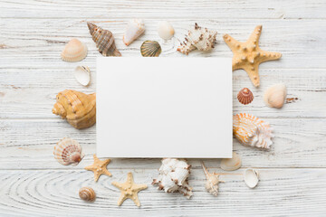 Summer time concept with blank greeting card and blank white paper on colored background. Seashells from ocean shore in the shape of frame separated with space for text top view