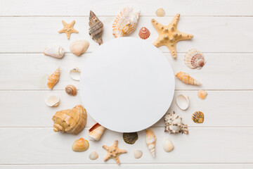 Summer time concept with blank greeting card and blank white paper on colored background. Seashells from ocean shore in the shape of frame separated with space for text top view