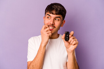 Young hispanic man holding keys car isolated on purple background relaxed thinking about something looking at a copy space.