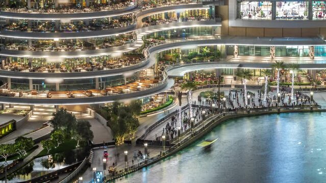 Shopping mall balcony with reataurants near fountain in Dubai downtown aerial night timelapse, United Arab Emirates. Illuminated waterfront walking area