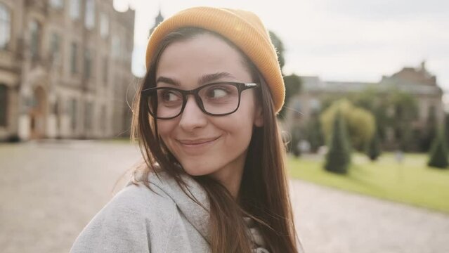 Happy cheerful young woman showing tongue giving wink on city street. Portrait of beautiful woman in yellow hat and glasses smiling outdoors. Urban lifestyle concept. Traveler
