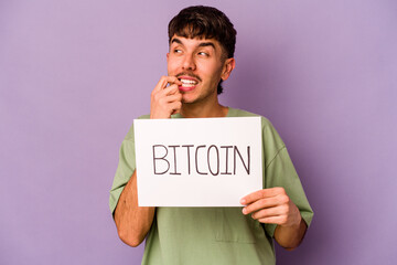 Young hispanic man holding bitcoin placard isolated on purple background relaxed thinking about something looking at a copy space.