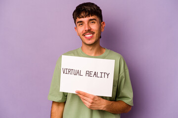 Young hispanic man holding virtual reality placard isolated on purple background happy, smiling and cheerful.