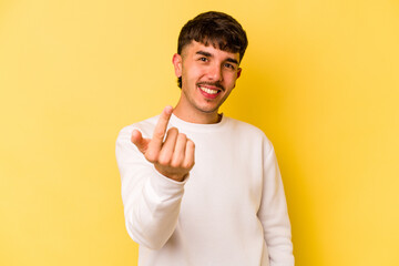 Young caucasian man isolated on yellow background pointing with finger at you as if inviting come closer.