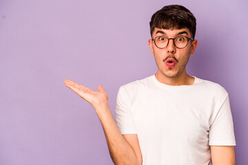 Fototapeta premium Young caucasian man isolated on purple background impressed holding copy space on palm.