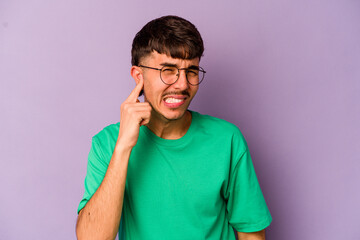 Young caucasian man isolated on purple background covering ears with hands.
