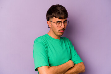 Young caucasian man isolated on purple background suspicious, uncertain, examining you.