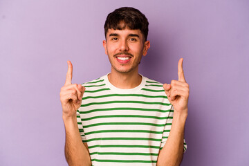 Young caucasian man isolated on purple background indicates with both fore fingers up showing a blank space.