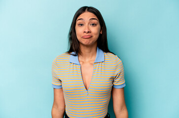 Young hispanic woman isolated on blue background shrugs shoulders and open eyes confused.