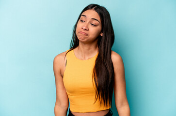 Young hispanic woman isolated on blue background shrugs shoulders and open eyes confused.