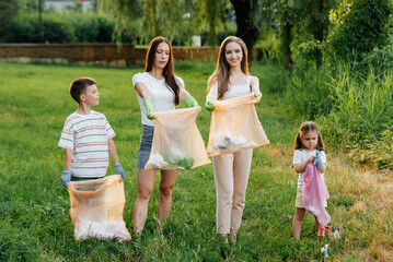 Fototapeta premium A group of adults and children together at sunset is engaged in garbage collection in the park. Environmental care, waste recycling. Sorting garbage.