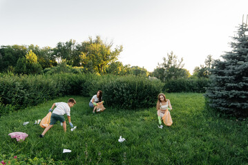 A group of adults and children together at sunset is engaged in garbage collection in the park....