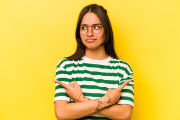 Young hispanic woman isolated on yellow background points sideways, is trying to choose between two...