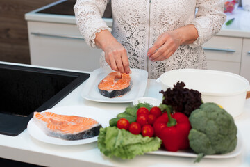 The hands of a retired woman cook red salmon fish in the kitchen, salt it and add spices