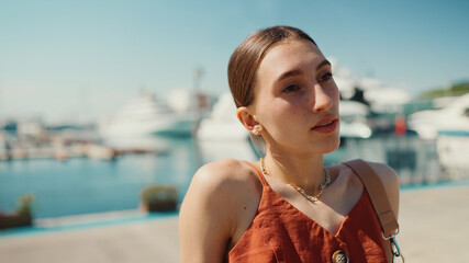 Smiling woman posing for the camera in the sea port. Girl enjoys a warm sunny day on background of yachts and ships