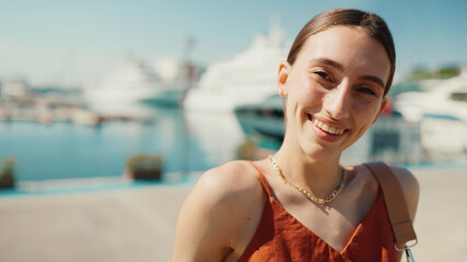 Smiling woman posing for the camera in the sea port. Girl enjoys a warm sunny day on background of...