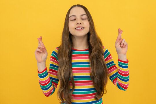 Portrait of adorable little teenager gitl standing with closed eyes and crossing fingers, wishing for good luck. Childhood dreams and hopes.
