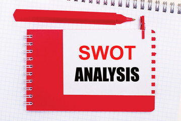 On a white notepad, a red pen, a red notepad and a white sheet of paper with the text SWOT ANALYSIS