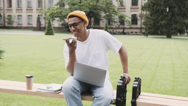 Young African American student sitting and studying in the campus talking on the phone with a smile.