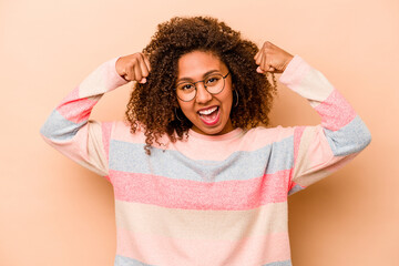 Young African American woman isolated on beige background showing strength gesture with arms, symbol of feminine power
