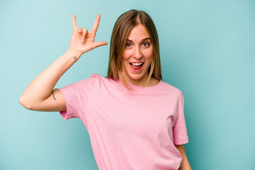 Young caucasian woman isolated on blue background showing a horns gesture as a revolution concept.