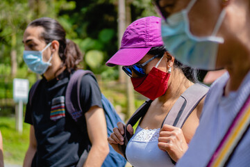 young latin woman with red cloth mask, surrounded by people with disposable medical masks in a natural park, tropical climate.