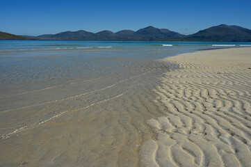 Luskentyre beach, Isle of Harris. Blue sky, mountains in background, sea and wavy lines of sand in foreground. No people. Tranquil, summer scene.