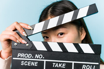 Young asian woman holding a clapperboard isolated on blue background