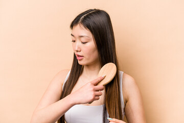 Naklejka premium Young asian woman combing her hair isolated on beige background