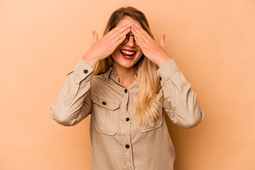 Young caucasian woman isolated on beige background covers eyes with hands, smiles broadly waiting for a surprise.